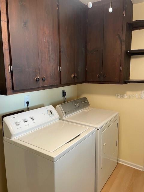 laundry area with light wood-type flooring, washing machine and dryer, and cabinets