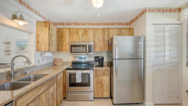 kitchen featuring light stone counters, sink, ceiling fan, and stainless steel appliances