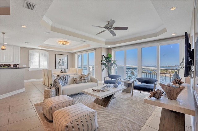 living room with ceiling fan, light tile patterned flooring, crown molding, and a tray ceiling