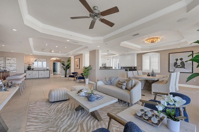 tiled living room with a raised ceiling, ceiling fan, and ornamental molding