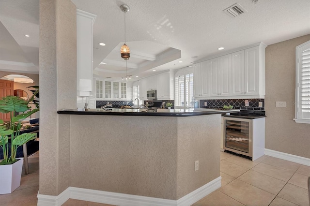 kitchen featuring beverage cooler, kitchen peninsula, pendant lighting, a tray ceiling, and white cabinets