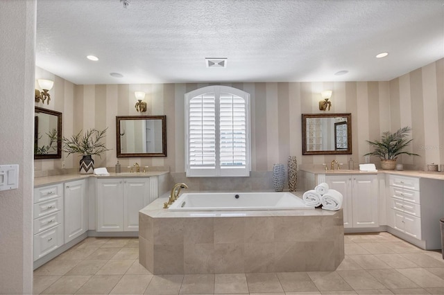 bathroom featuring tiled tub, tile patterned flooring, vanity, and a textured ceiling