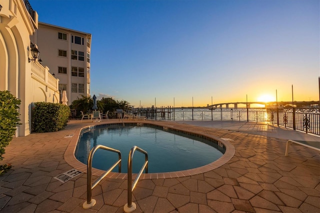 pool at dusk featuring a patio area and a water view