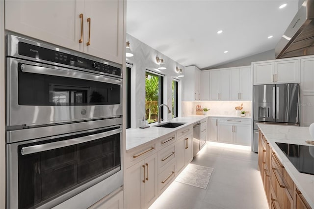 kitchen with sink, wall chimney exhaust hood, light stone countertops, white cabinetry, and stainless steel appliances