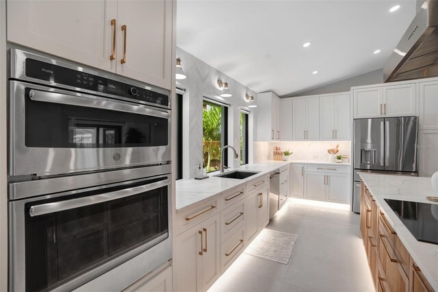 1899 Buccaneer Cir, Sarasota, FL 34231 - kitchen with appliances with stainless steel finishes, wall chimney range hood, vaulted ceiling, tasteful backsplash, and light stone countertops