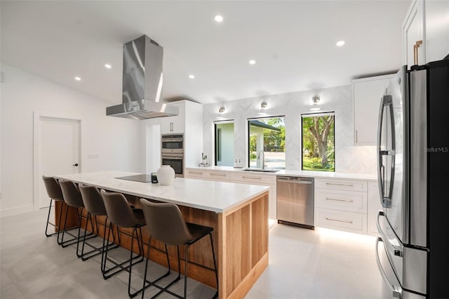 kitchen featuring appliances with stainless steel finishes, wall chimney range hood, white cabinets, a center island, and lofted ceiling