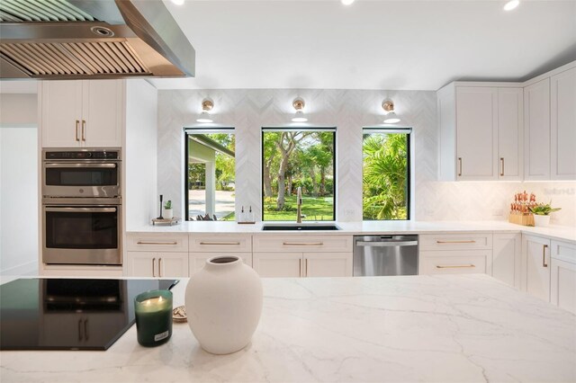 1899 Buccaneer Cir, Sarasota, FL 34231 - kitchen featuring appliances with stainless steel finishes, wall chimney exhaust hood, light stone countertops, decorative backsplash, and white cabinets