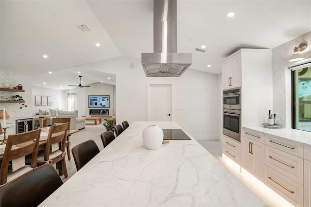 kitchen with white cabinets, light stone counters, a breakfast bar area, and exhaust hood