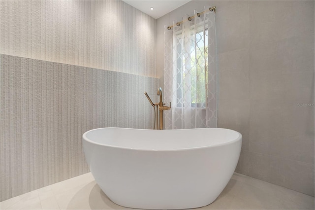 bathroom with tile patterned flooring, a bathtub, tile walls, and a wealth of natural light