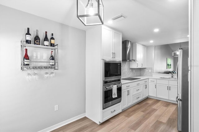 kitchen featuring sink, light hardwood / wood-style flooring, appliances with stainless steel finishes, wall chimney range hood, and white cabinets