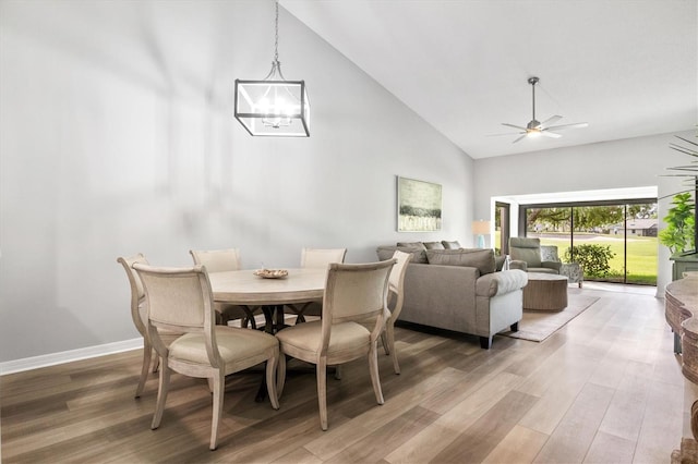 dining area with ceiling fan with notable chandelier, high vaulted ceiling, and hardwood / wood-style floors