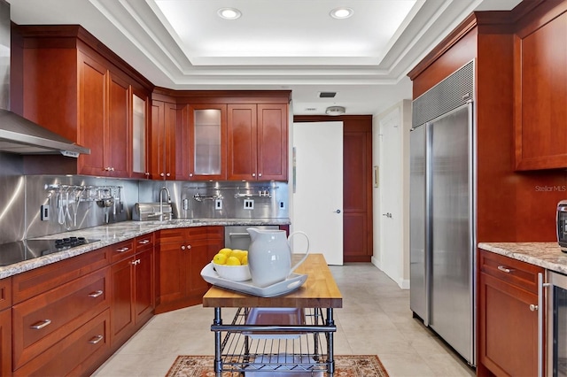 kitchen featuring sink, wall chimney exhaust hood, stainless steel appliances, light stone counters, and backsplash