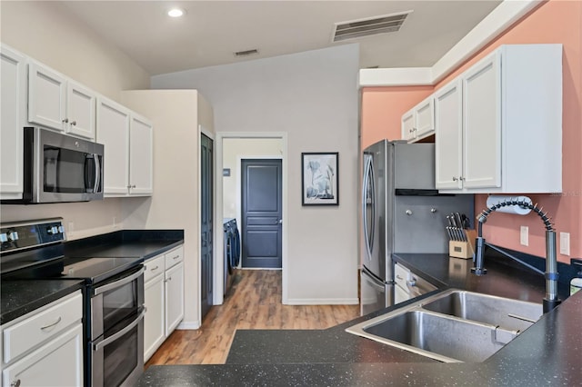 kitchen with white cabinets, stainless steel appliances, vaulted ceiling, and light hardwood / wood-style floors