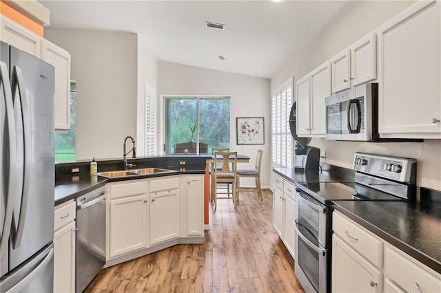 kitchen with sink, light hardwood / wood-style flooring, vaulted ceiling, white cabinetry, and stainless steel appliances