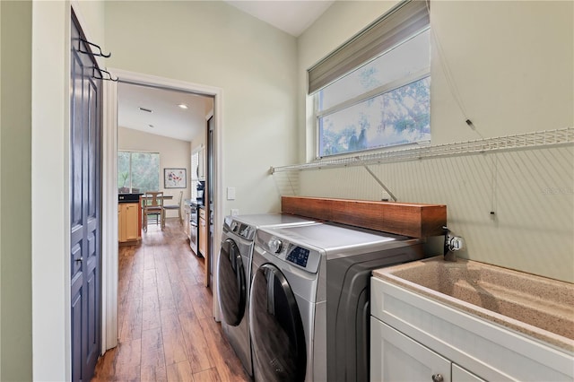 clothes washing area featuring washer and dryer, wood-type flooring, and cabinets