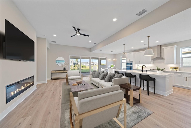 living room with ceiling fan with notable chandelier, a healthy amount of sunlight, sink, and light hardwood / wood-style flooring