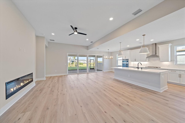 unfurnished living room featuring plenty of natural light, ceiling fan, sink, and light hardwood / wood-style flooring