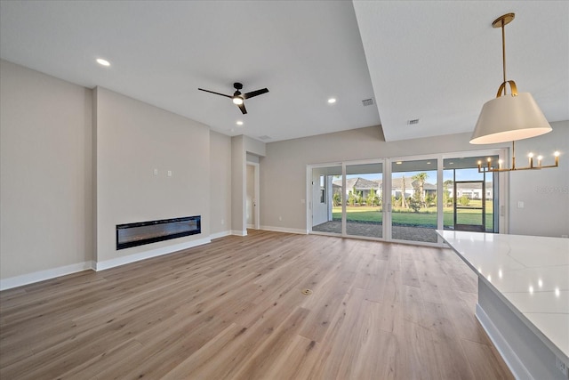 unfurnished living room with ceiling fan with notable chandelier and light wood-type flooring