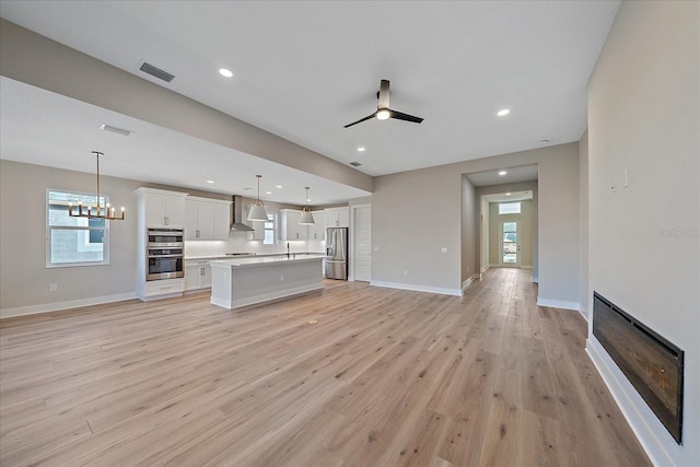 unfurnished living room with ceiling fan with notable chandelier, light hardwood / wood-style flooring, and sink