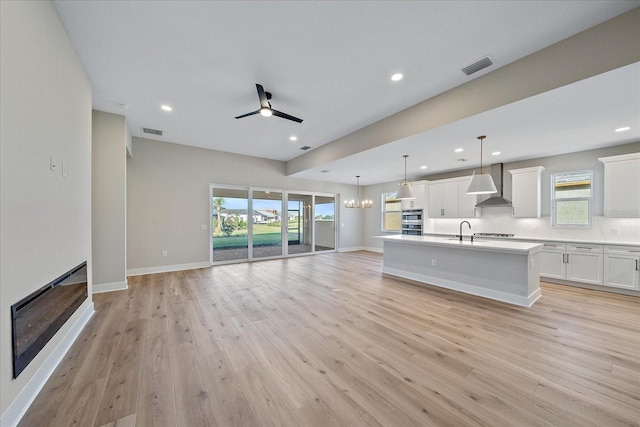 unfurnished living room with ceiling fan with notable chandelier, sink, and light hardwood / wood-style flooring