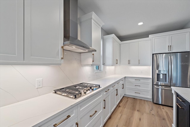 kitchen with light hardwood / wood-style flooring, wall chimney exhaust hood, appliances with stainless steel finishes, tasteful backsplash, and white cabinetry