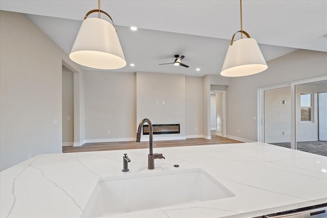 kitchen with ceiling fan, sink, hanging light fixtures, light stone counters, and wood-type flooring