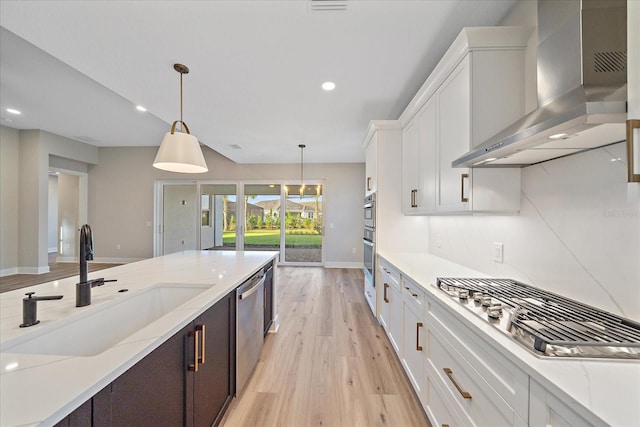 kitchen featuring white cabinets, wall chimney range hood, stainless steel appliances, and light hardwood / wood-style flooring