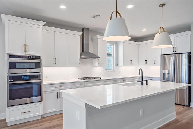 kitchen featuring pendant lighting, sink, wall chimney exhaust hood, appliances with stainless steel finishes, and white cabinetry