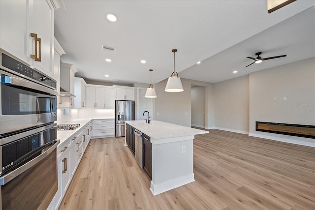 kitchen featuring white cabinetry, light hardwood / wood-style flooring, pendant lighting, a kitchen island with sink, and appliances with stainless steel finishes