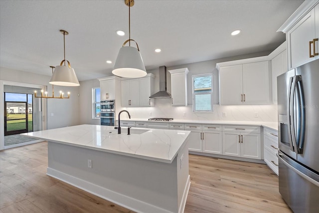 kitchen with white cabinetry, a center island with sink, wall chimney exhaust hood, and appliances with stainless steel finishes