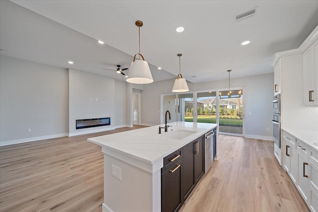 kitchen featuring white cabinets, a center island with sink, sink, and hanging light fixtures