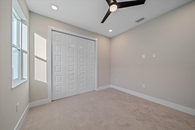 unfurnished bedroom featuring ceiling fan, light colored carpet, and a closet