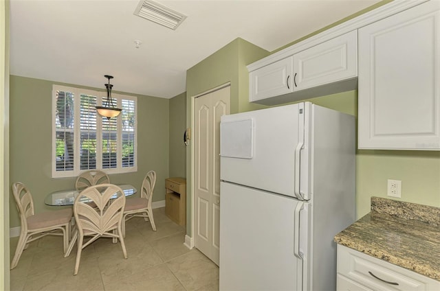 kitchen featuring pendant lighting, white cabinets, white refrigerator, light tile patterned floors, and stone countertops