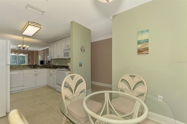 kitchen with white appliances, light tile patterned floors, pendant lighting, a notable chandelier, and white cabinetry