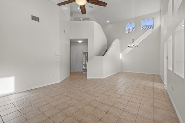 unfurnished living room with a towering ceiling, light tile patterned flooring, and ceiling fan with notable chandelier