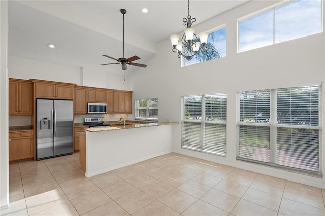 kitchen featuring pendant lighting, a high ceiling, light tile patterned floors, appliances with stainless steel finishes, and light stone counters