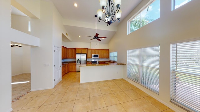 kitchen featuring hanging light fixtures, a high ceiling, kitchen peninsula, light tile patterned floors, and appliances with stainless steel finishes