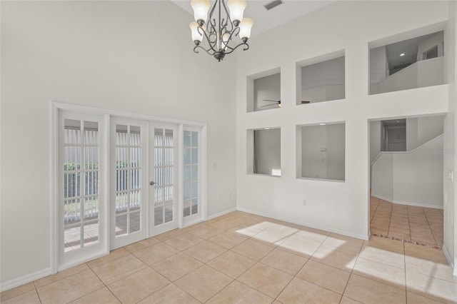 empty room with a towering ceiling, light tile patterned floors, ceiling fan with notable chandelier, and french doors