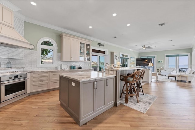 kitchen featuring oven, light wood-type flooring, an island with sink, and a wealth of natural light