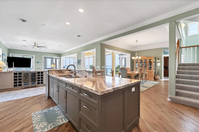 kitchen featuring pendant lighting, ceiling fan with notable chandelier, sink, light stone countertops, and light wood-type flooring