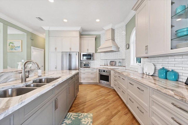 kitchen with light stone countertops, white cabinetry, sink, stainless steel appliances, and custom exhaust hood