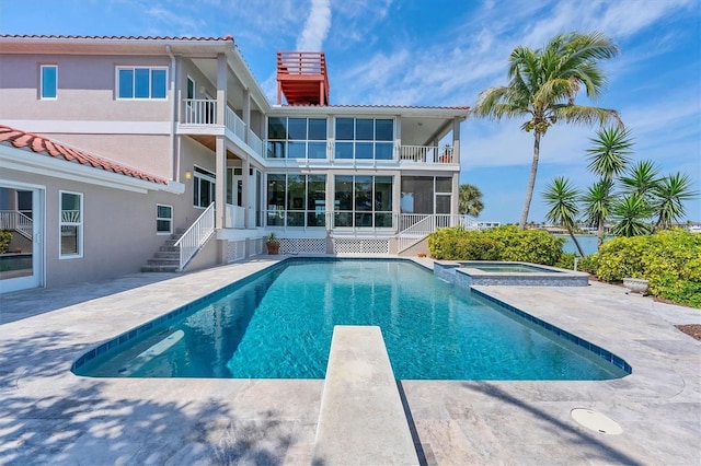 rear view of property with a pool with hot tub, a balcony, and a patio