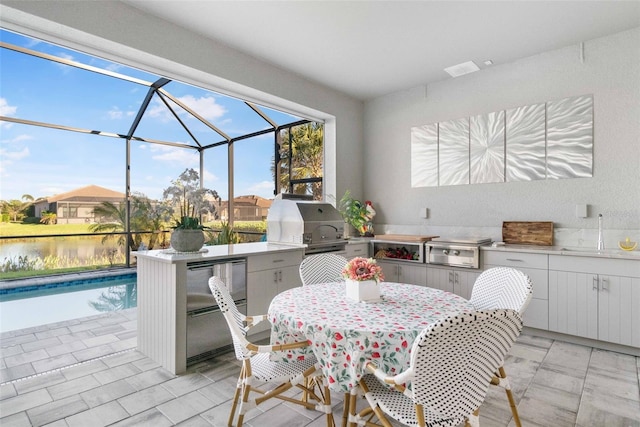 view of patio with a grill, a water view, a lanai, and exterior kitchen