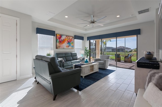 living room with light hardwood / wood-style floors, a raised ceiling, and ceiling fan