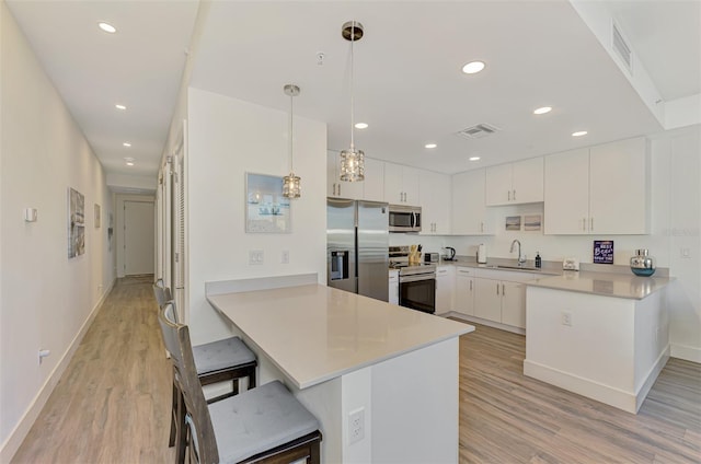 kitchen with white cabinets, a kitchen breakfast bar, hanging light fixtures, appliances with stainless steel finishes, and kitchen peninsula