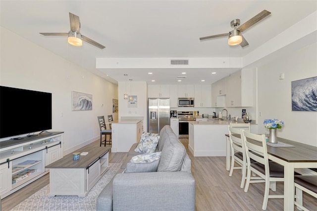 living room with ceiling fan, sink, and light wood-type flooring