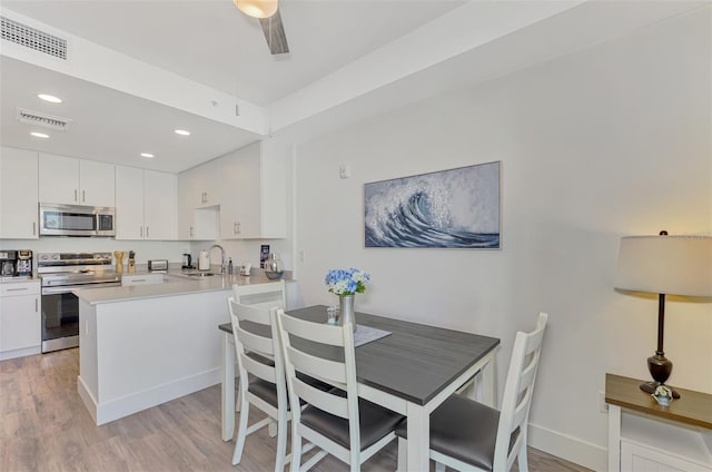 kitchen featuring sink, light hardwood / wood-style flooring, white cabinetry, kitchen peninsula, and stainless steel appliances