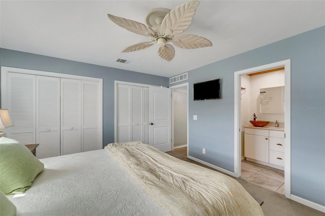 bedroom featuring ceiling fan, ensuite bathroom, and multiple closets