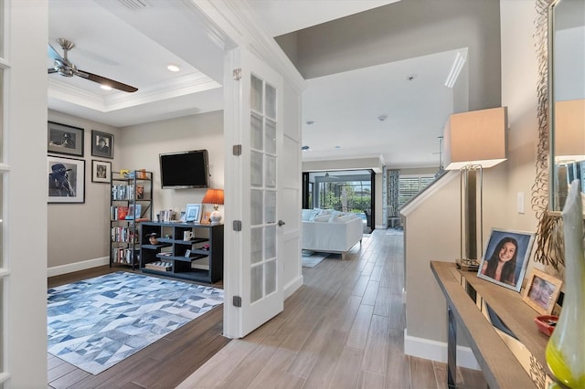 corridor featuring a raised ceiling, light wood-type flooring, ornamental molding, and french doors