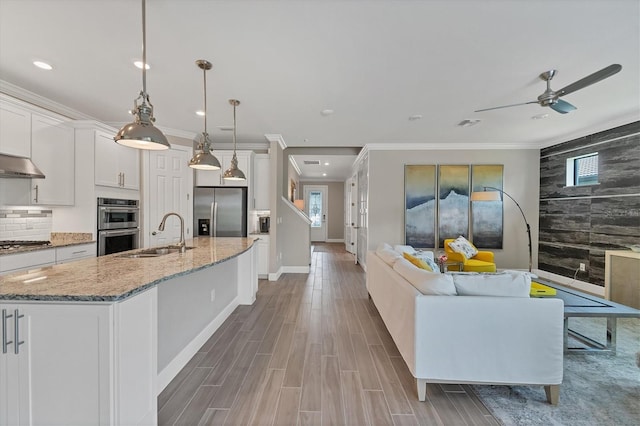 kitchen with stainless steel appliances, sink, decorative light fixtures, a center island with sink, and white cabinets